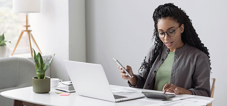 woman accountant with bachelors checks data accuracy on mobile and calculator