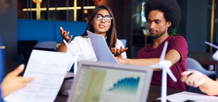 a woman goes over information with coworkers while another person tracks details on a chart on a laptop