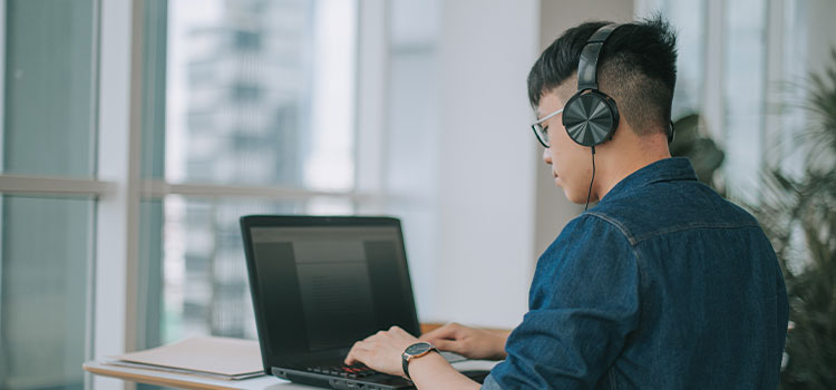 A man wearing headphones types on his laptop