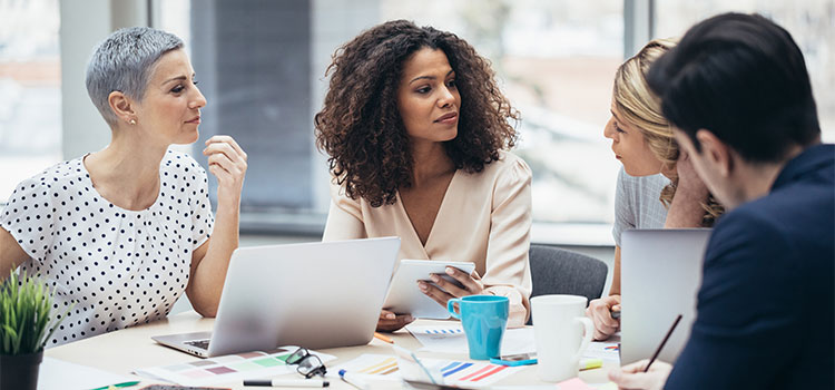 A woman discusses information on a laptop and paper with three other professionals at a table.