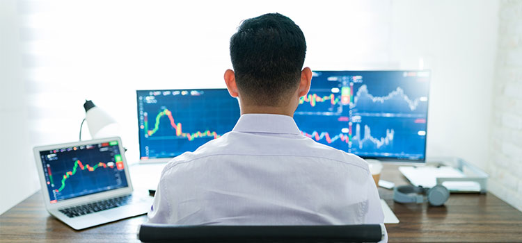 A professional man examines data charts on three computer screens