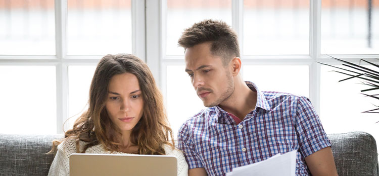 A man and a woman sit on a couch as they look at information online