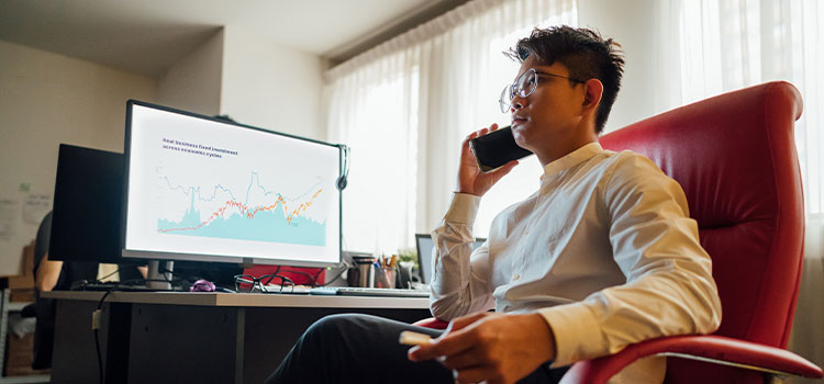 A man with a laptop that displays financial charts talks on the phoneht