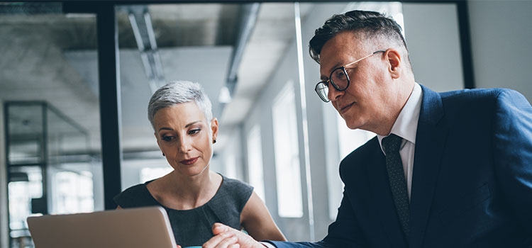 A man and a woman in an office discuss information on a laptop