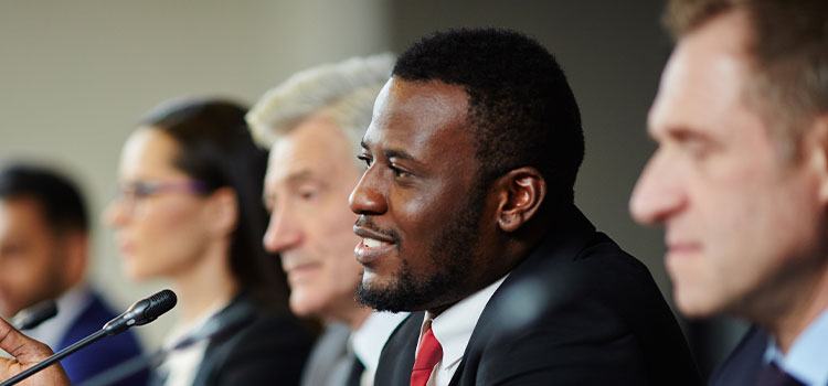 Businessmen talk at a table with microphones and flags