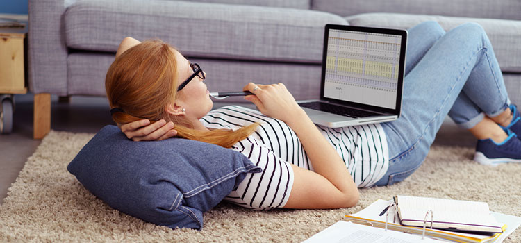 Woman reads on laptop while lying on the floor