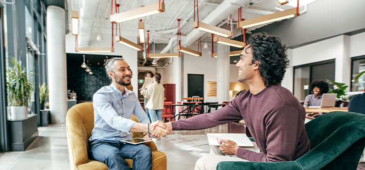 Two men shake hands as they sit together