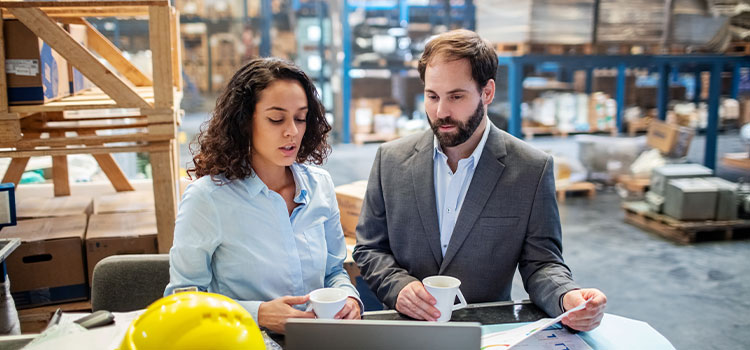 a man and a woman in a warehouse review information on a laptop