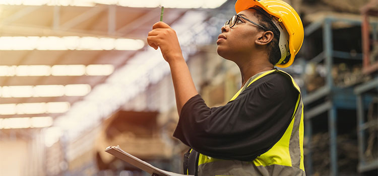 a woman wearing a hardhat surveys goods in a warehouse